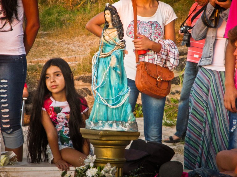 Ya habían armado la ofrenda. La imagen de Iemanyá con su traje azul celeste que llega hasta el piso, lanzando perlas de sus manos lucía en todo su esplendor; a sus pies la barcaza azul la cual sería arrojada al mar al final de la ceremonia, en ella se guardaban los pedidos de sus fieles, cartas solicitando sus favores o agradecimientos por haberlos concedidos, perfumes, joyas, velas, jabones, etc. La barcaza estaba rodeada de flores blancas, palomitas de maíz, frutas